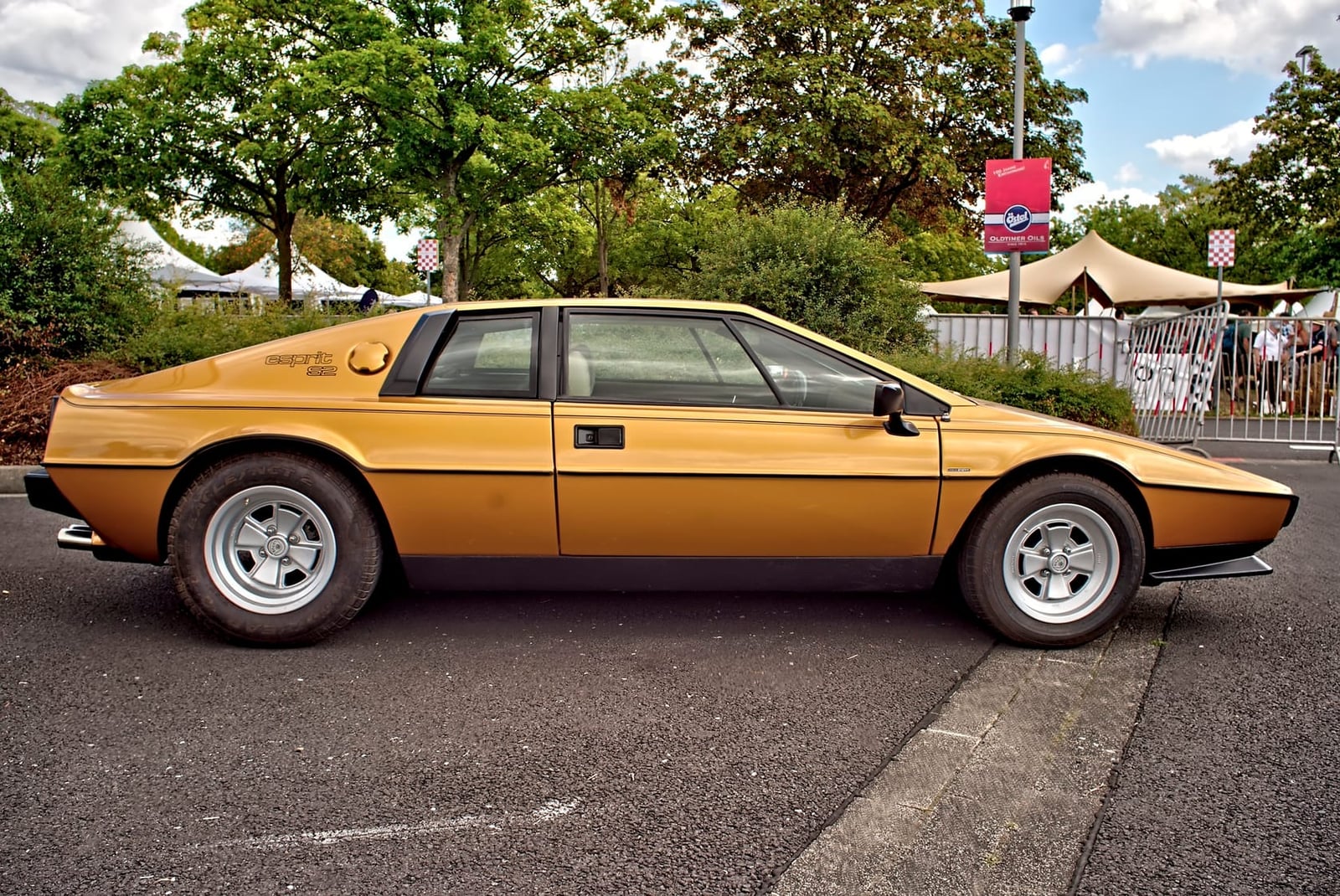 A gold 1979 Lotus Esprit S2 in profile, parked on tarmac at a show