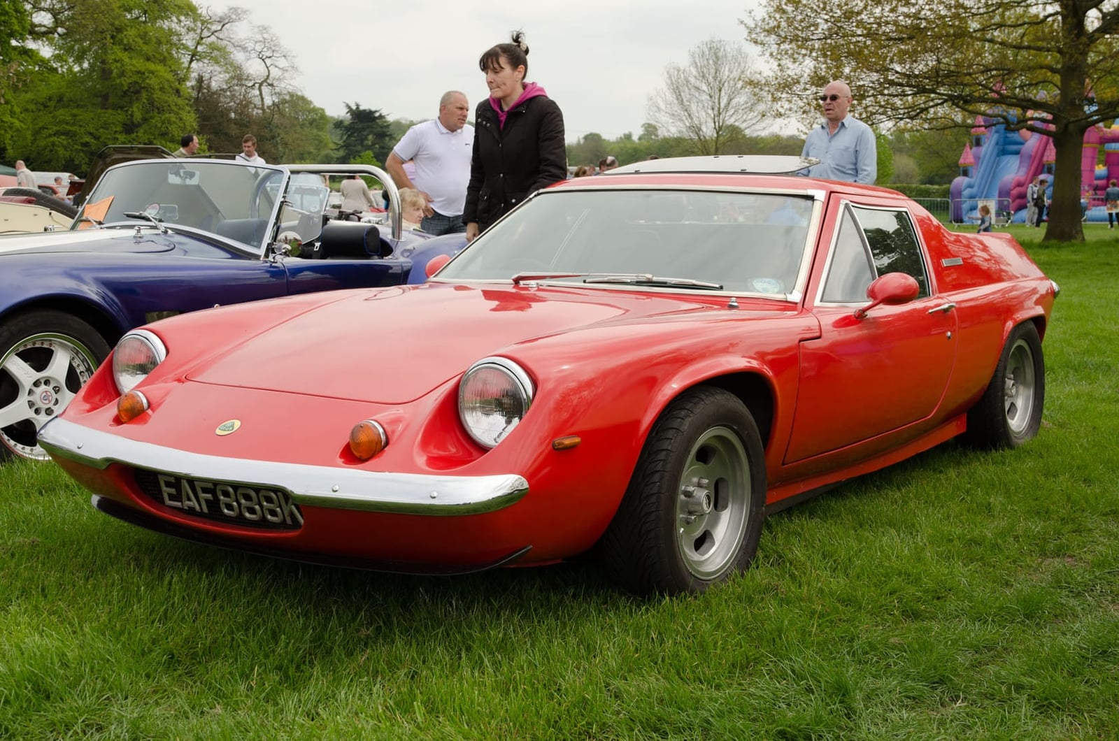 A red Lotus Europa Twin Cam on grass at a classic car show, front three-quarter view, UK registration EAF 889N