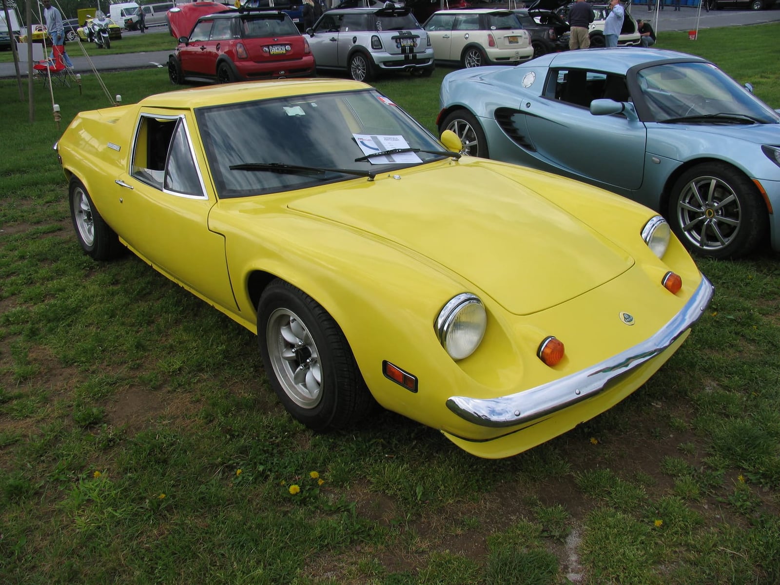 A yellow Lotus Europa Special on grass at a classic car gathering, front three-quarter view