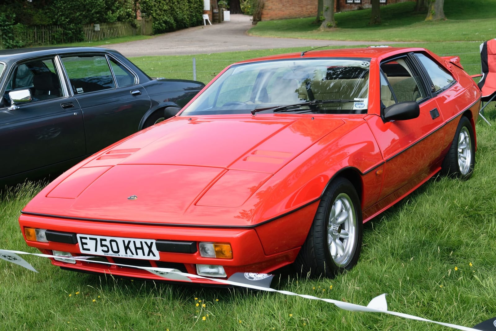 A white Lotus Excel with gold coachlines and gold wheels parked on a street, front three-quarter view, UK registration E747 DTF