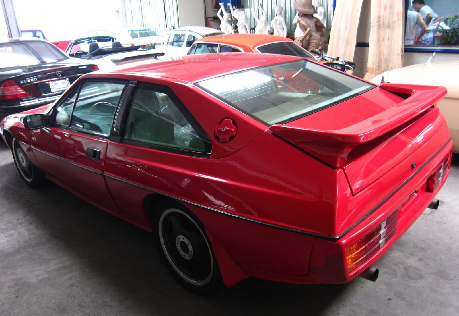 The rear three-quarter of a red Lotus Excel SE with rear spoiler, displayed indoors