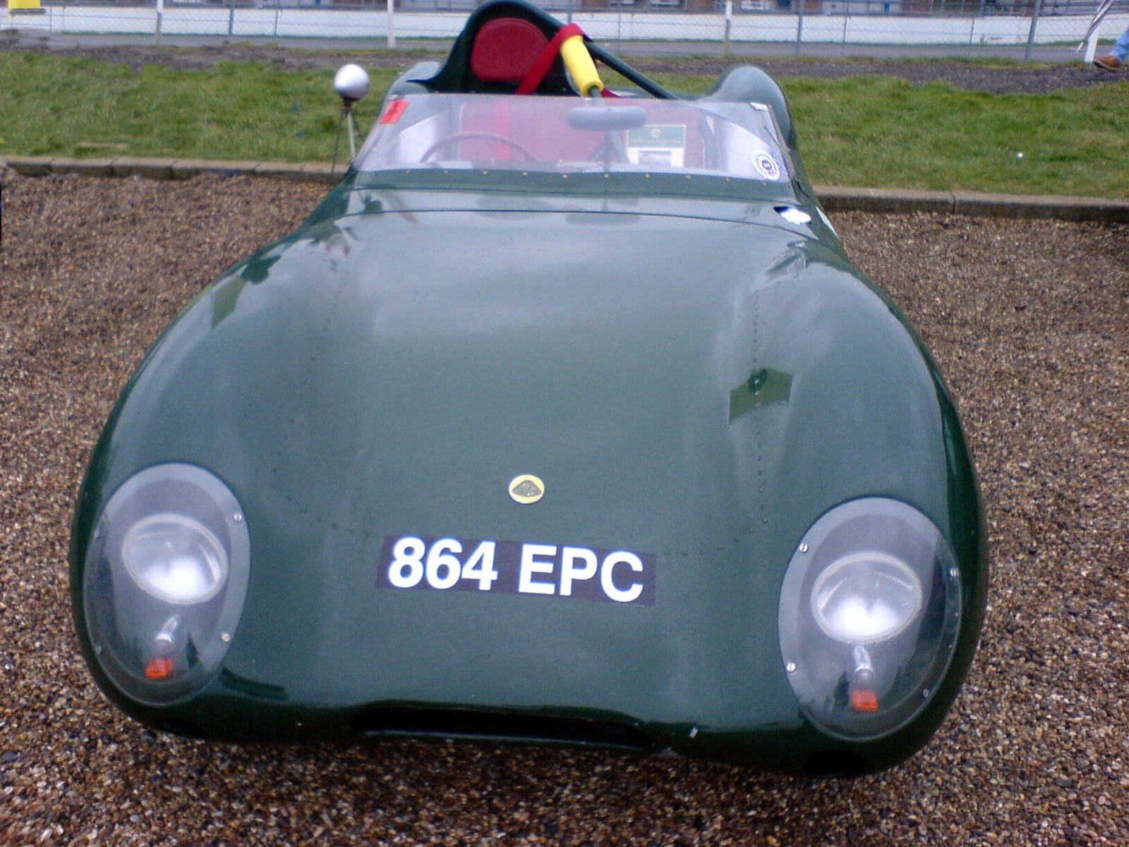 A dark green Lotus Eleven photographed head-on, showing the low nose and faired headlamps, UK registration 864 EPC