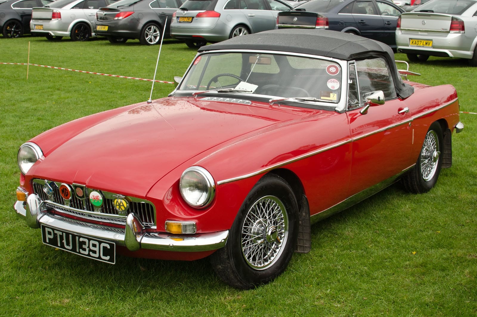 A red 1965 MG MGB roadster with chrome wire wheels and hood raised on a show field