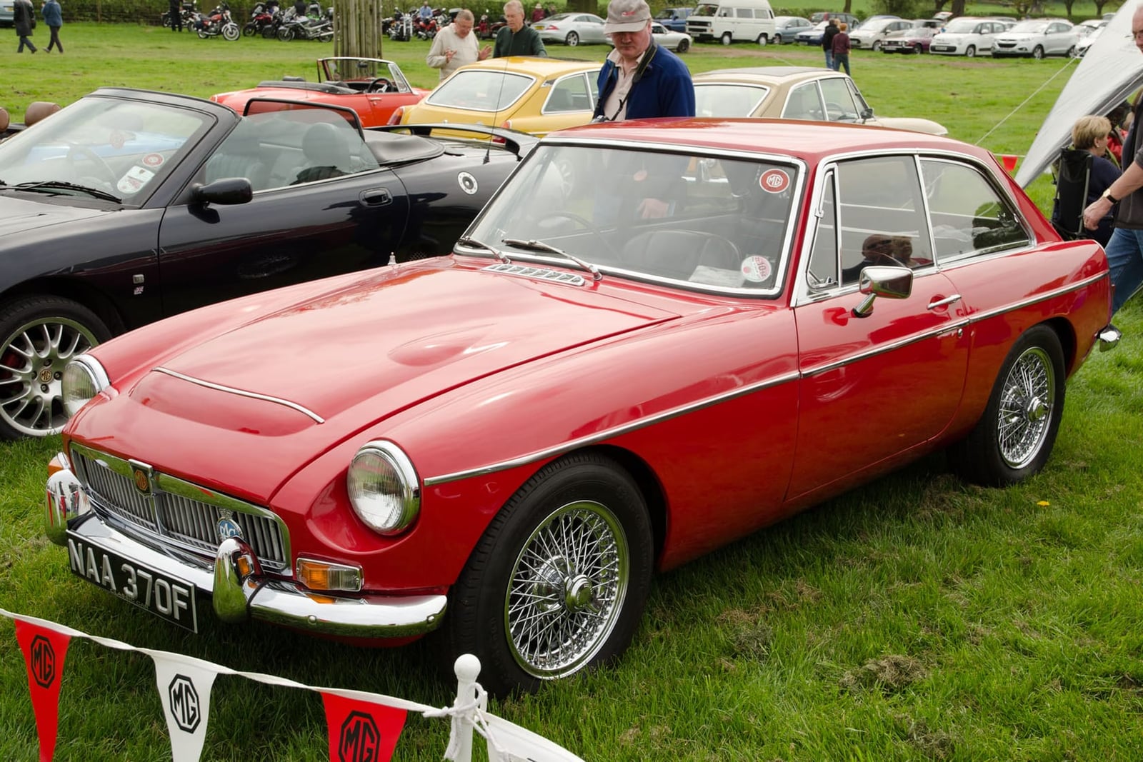 A red 1968 MGC GT with wire wheels and MG pennants at a club rally