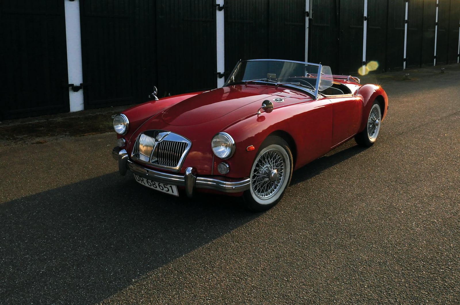 A red MG MGA roadster, front three-quarter view in evening light