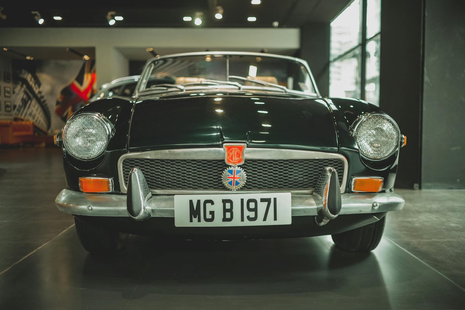 A British Racing Green MG MGB roadster, head-on front view under museum lighting