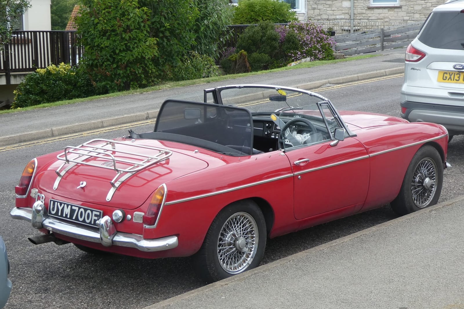 The rear of a red 1968 MGC roadster with a luggage rack and wire wheels, its hood down