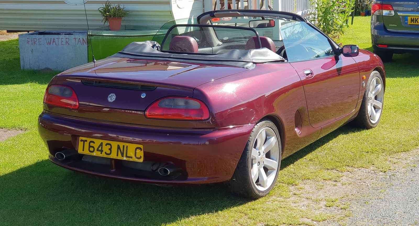 The rear of a maroon 1999 MGF anniversary edition with a UK registration on a show field