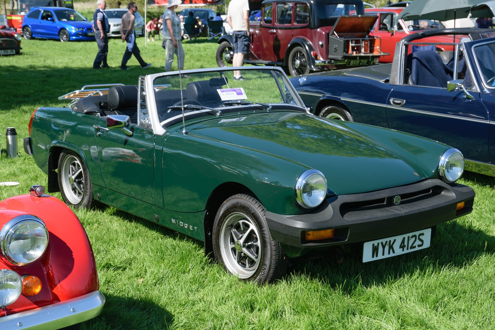 A British Racing Green MG Midget 1500 with black rubber bumpers, top down, front three-quarter view at a show