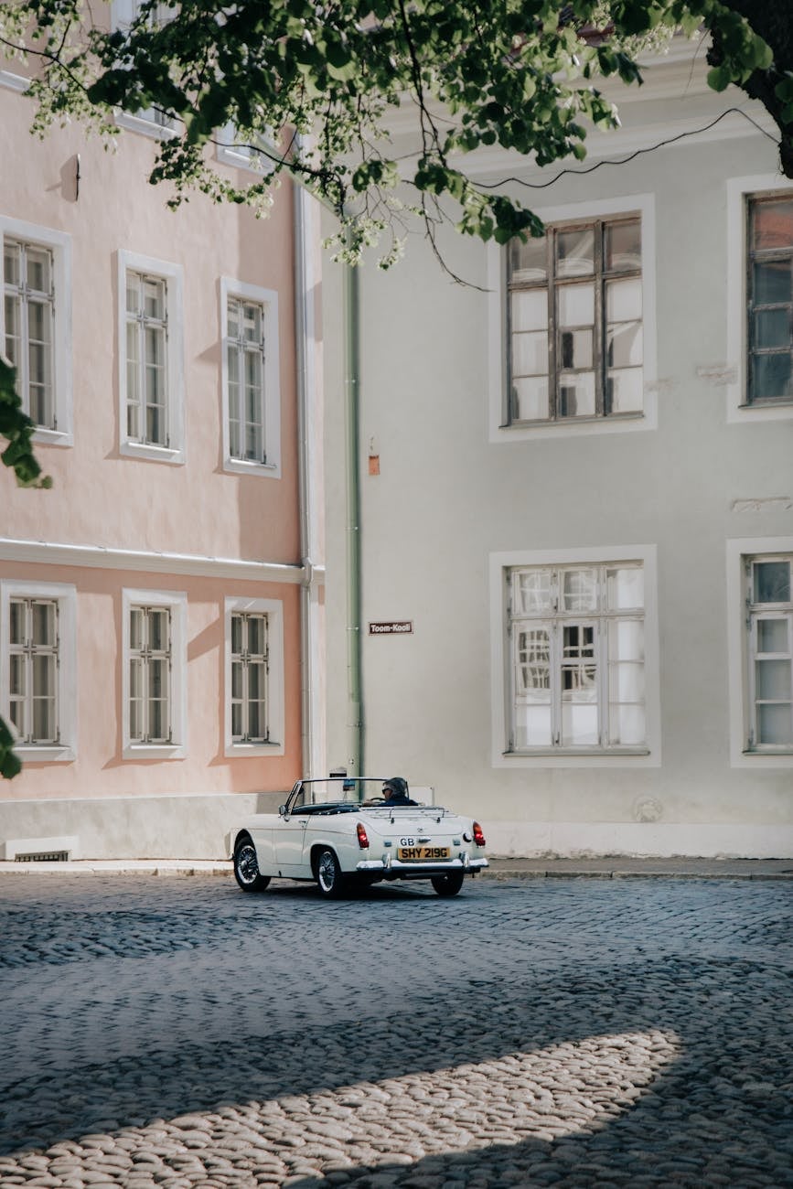 A white MG Midget being driven on a cobbled street in an old town