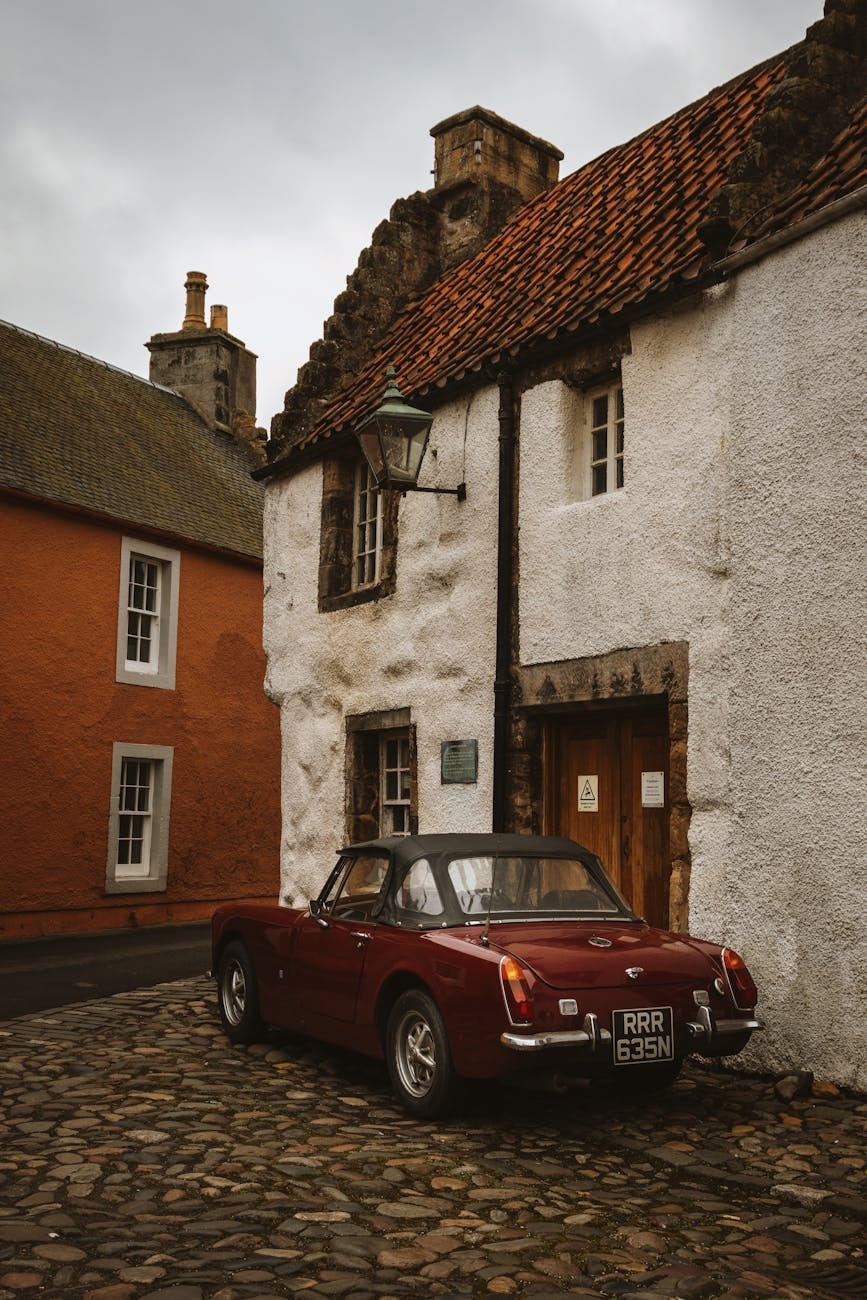 A maroon MG Midget parked in a cobbled lane