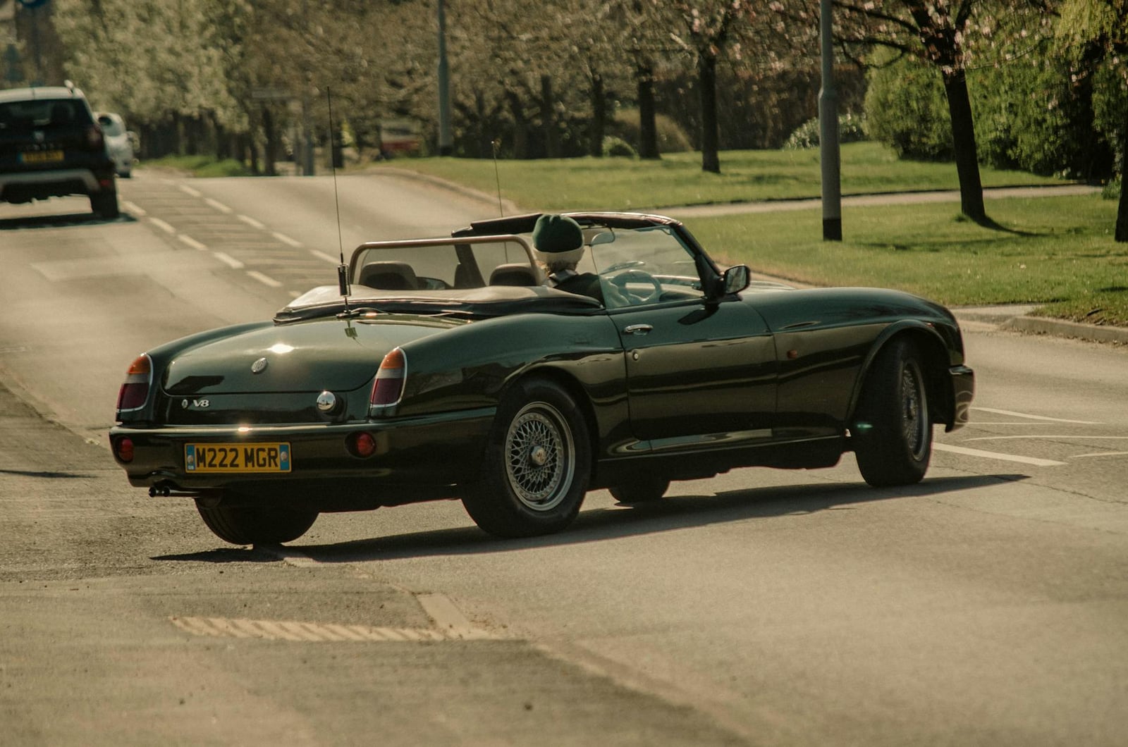 A British Racing Green MG RV8 being driven on a tree-lined road