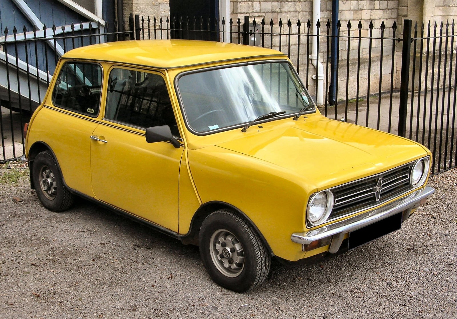 A yellow Mini 1275GT by railings, front three-quarter view