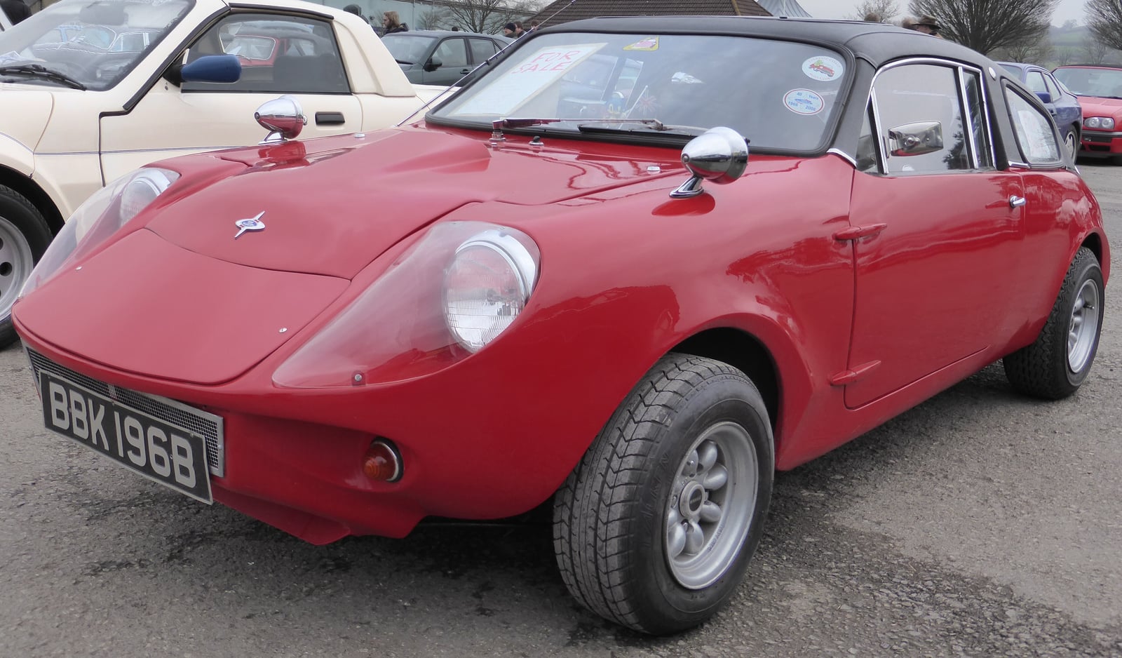 A red 1964 Mini Marcos, one of the earliest cars, photographed from the front at a classic car show