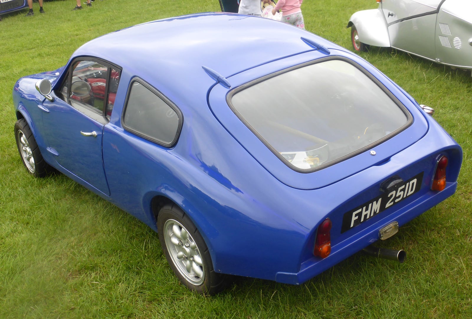 A blue 1966 Mini Marcos Mk1 coupe, rear three-quarter view on grass at a classic car show