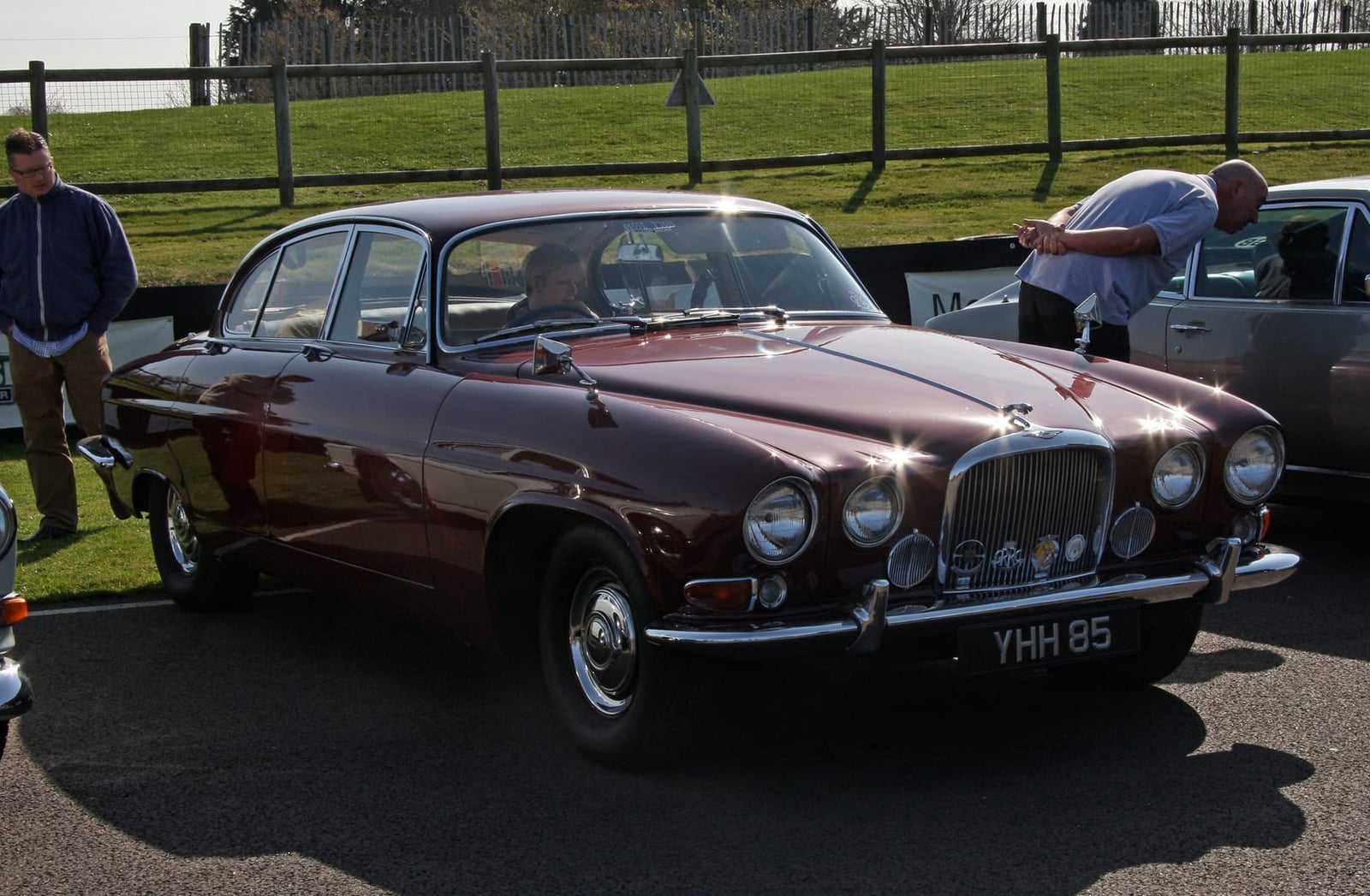 A maroon Jaguar Mk X saloon parked on tarmac at a classic car event, front three-quarter view, UK registration YHH 85
