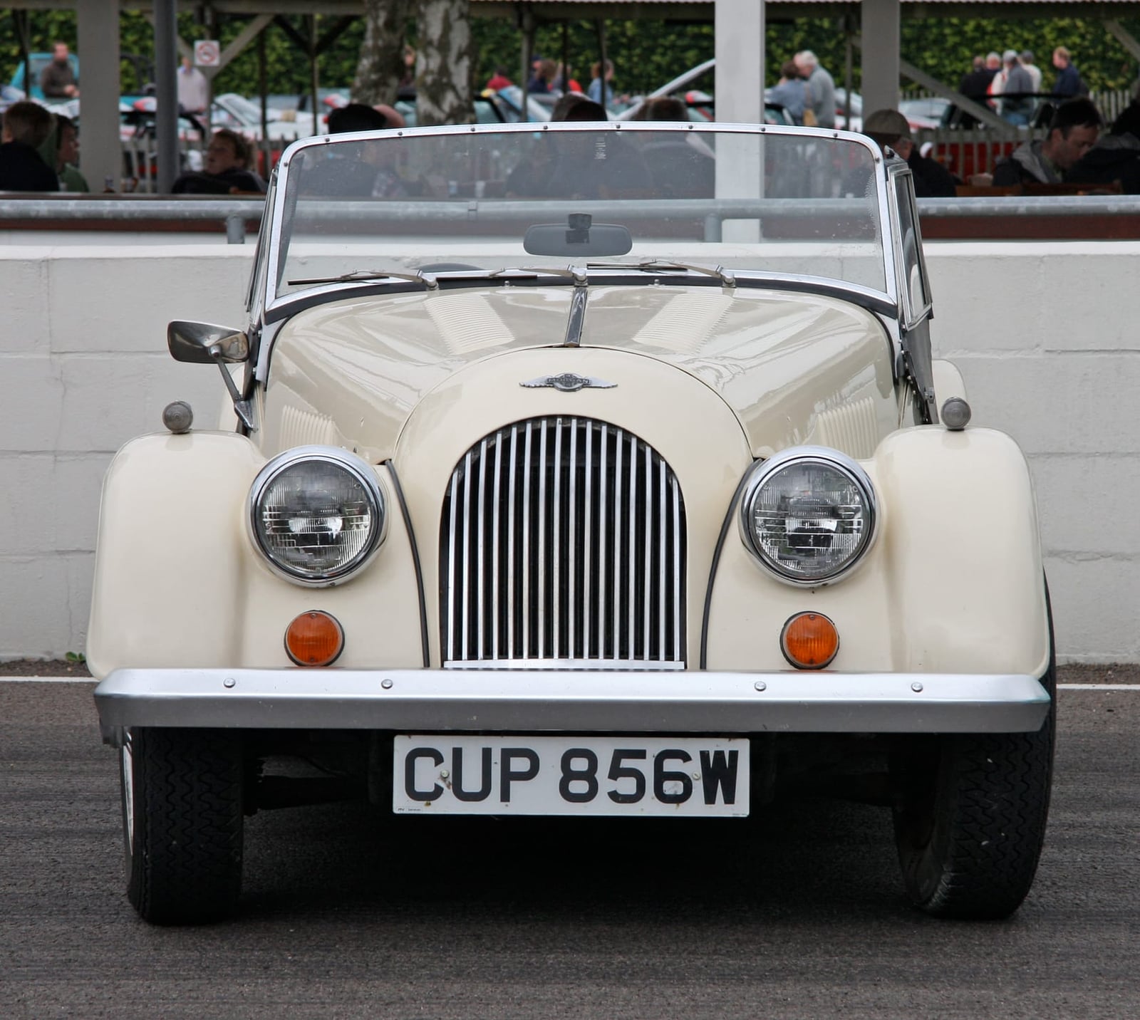 A cream Morgan roadster with a black-slatted chrome grille and separate front wings, photographed head-on in a circuit paddock