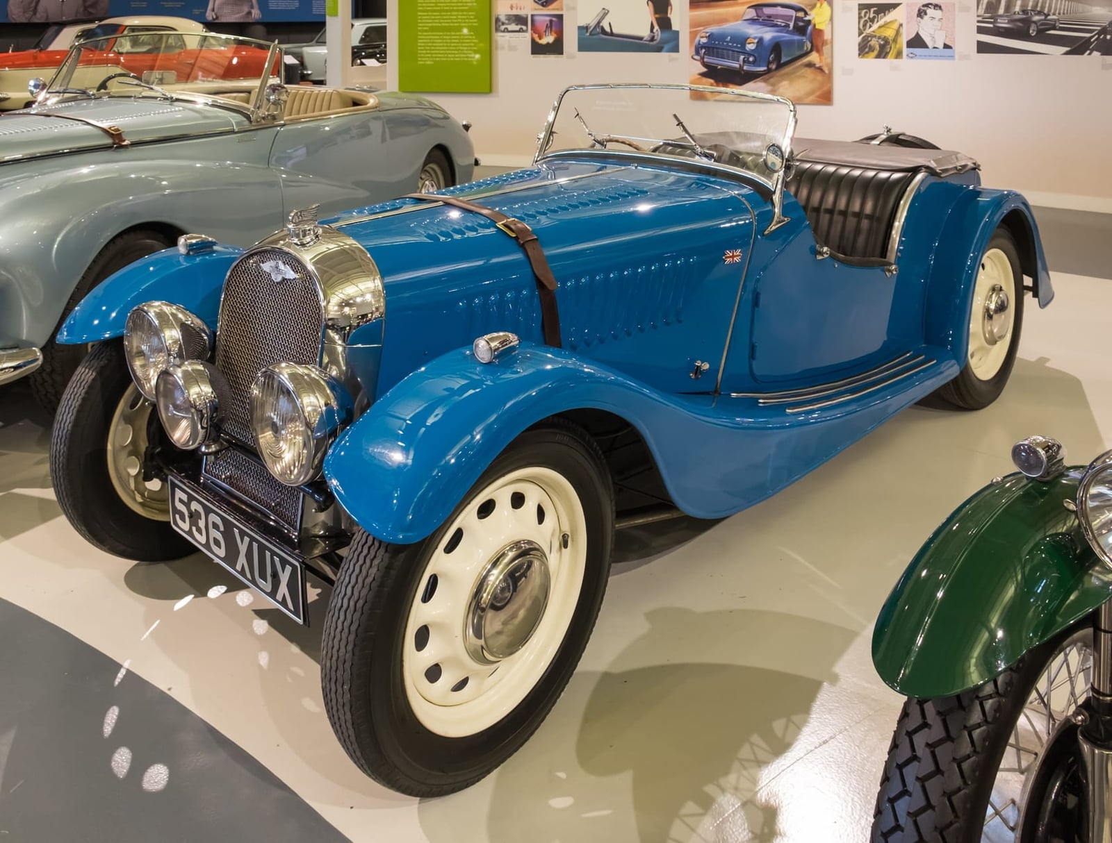 A blue 1939 Morgan 4/4 with cutaway doors and a folded windscreen on museum display, front three-quarter view, UK registration FSB XUX