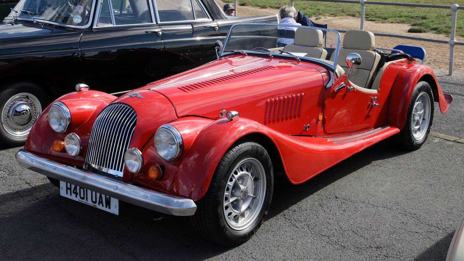 A red 1990 Morgan Plus 8 4.0 on grass at a classic car show, front three-quarter view, UK registration H401 UAW
