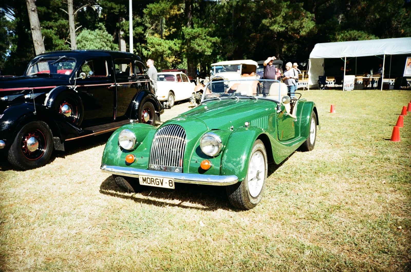 A green Morgan Plus 8 on grass at a classic car show, front three-quarter view, private registration MORGV 8