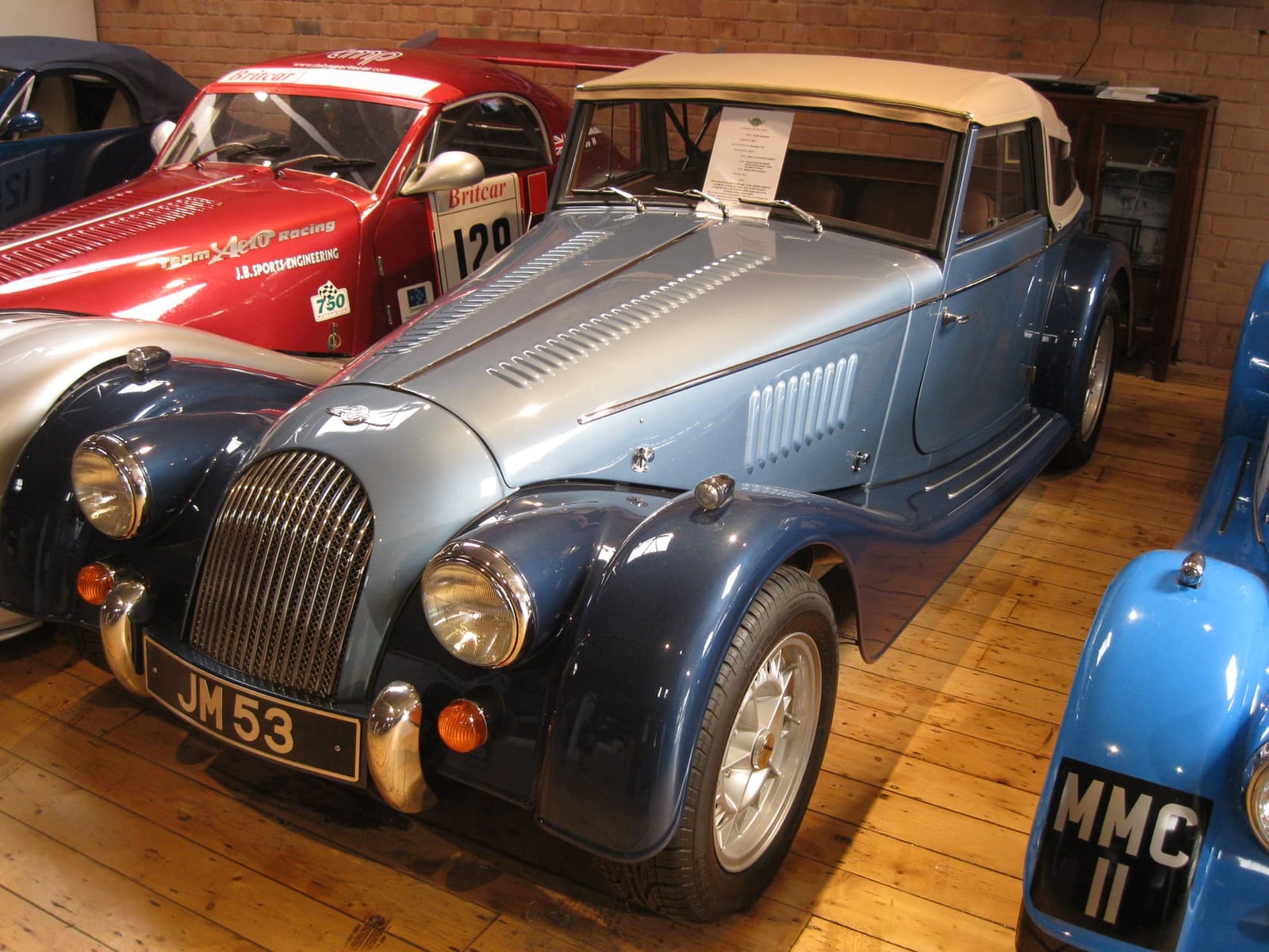 A silver and blue Morgan tourer carrying competition number 120 on indoor display, UK registration JM 53
