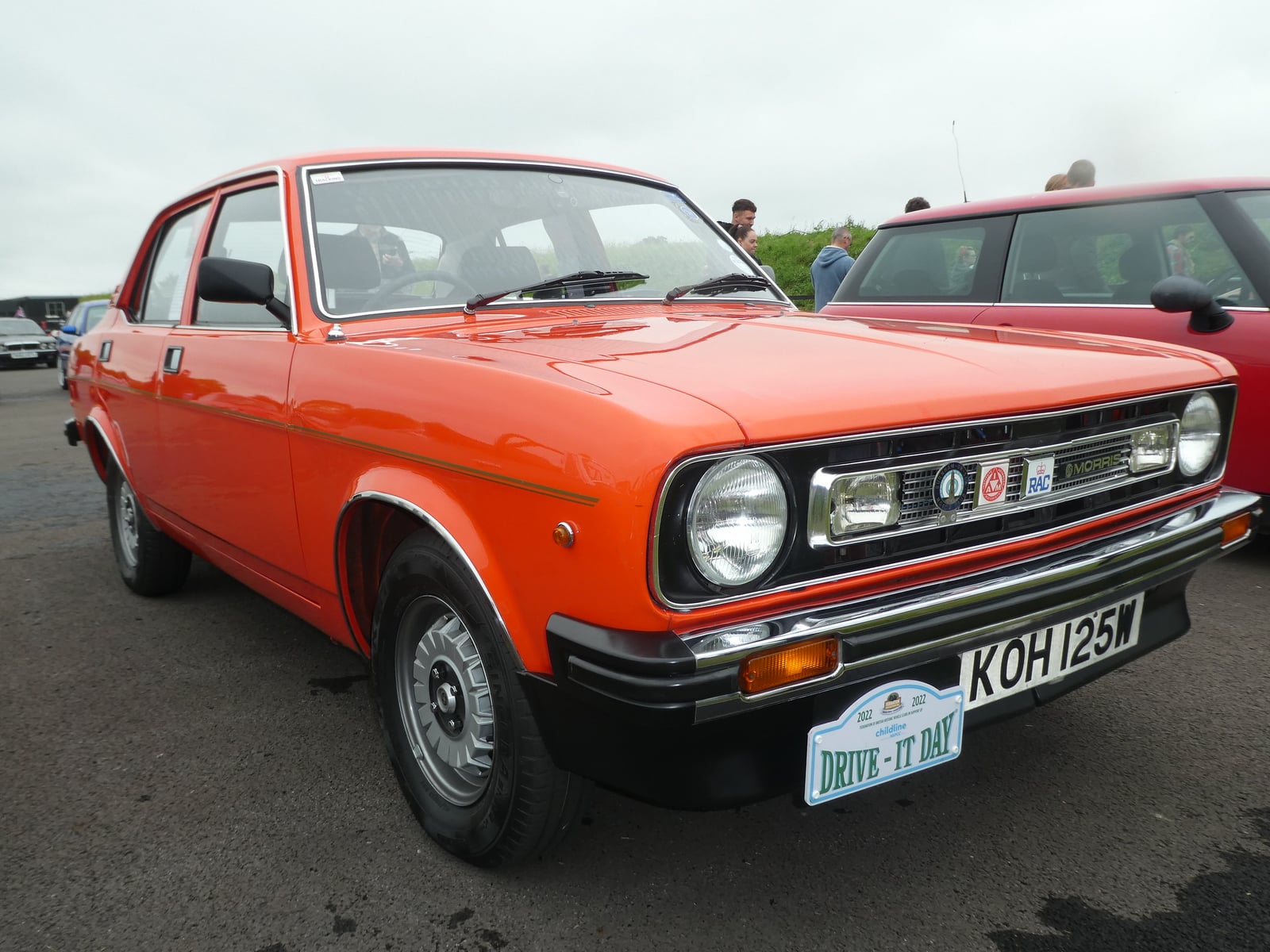 An orange Morris Marina two-door saloon, front three-quarter view at a classic car show, UK registration KOH 125W