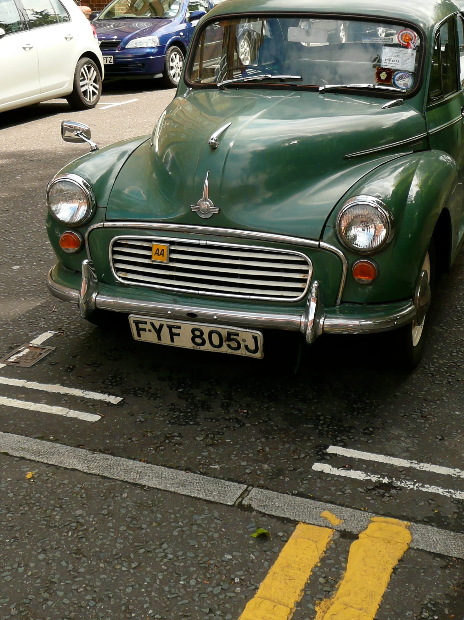 A dark green Morris Minor 1000 parked at the kerb on a British street beside double yellow lines, UK registration FYF 805J