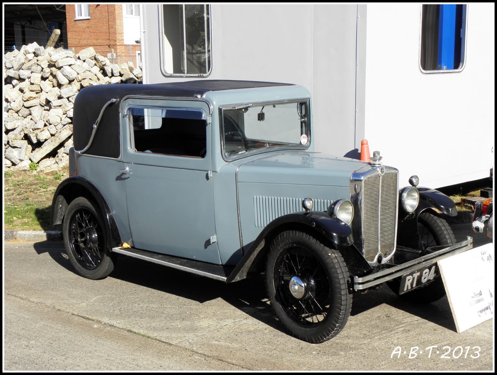 A black Morris Eight parked on a village street beside a brick building, UK registration FUW 458