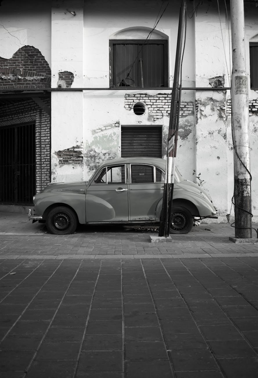 A black and white photograph of a Morris Minor saloon parked against a plain wall on a paved street