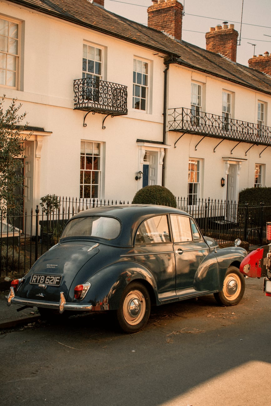 A pale green Morris Minor saloon parked outside a terrace of brick houses