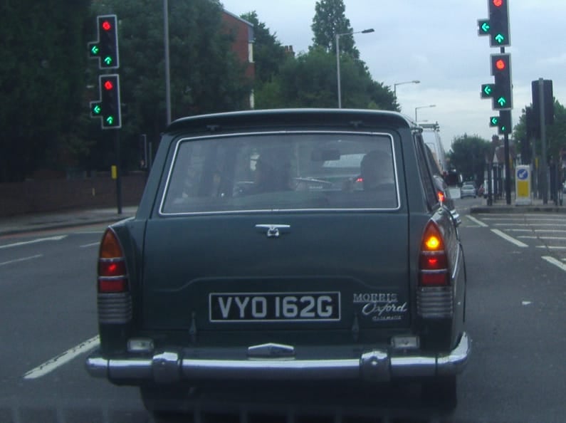 The rear of a dark Morris Oxford Traveller estate waiting at traffic lights