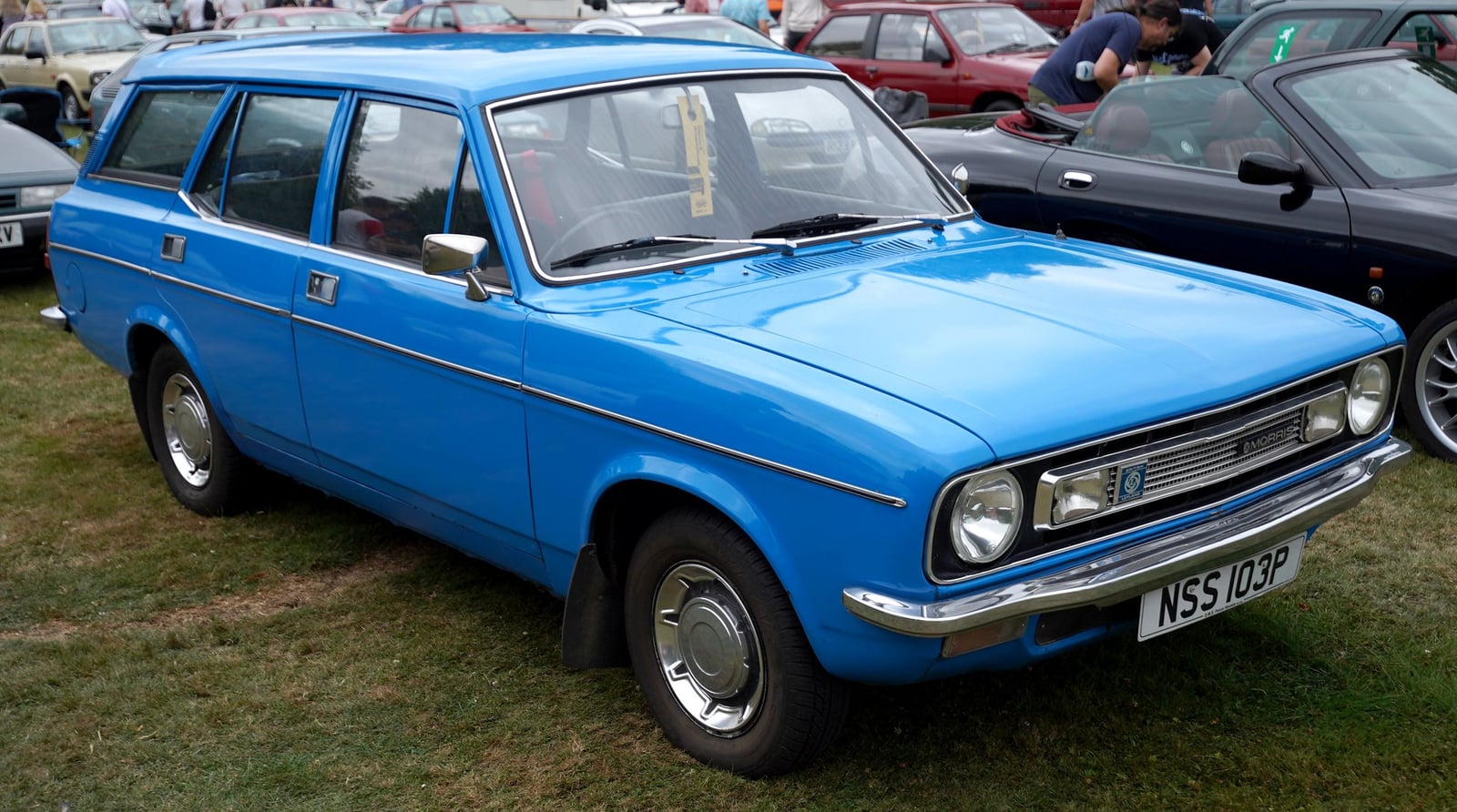A bright blue Morris Marina 1.8 SDL Estate (1975-76, NSS103P plate), front three-quarter view on grass at a classic car show