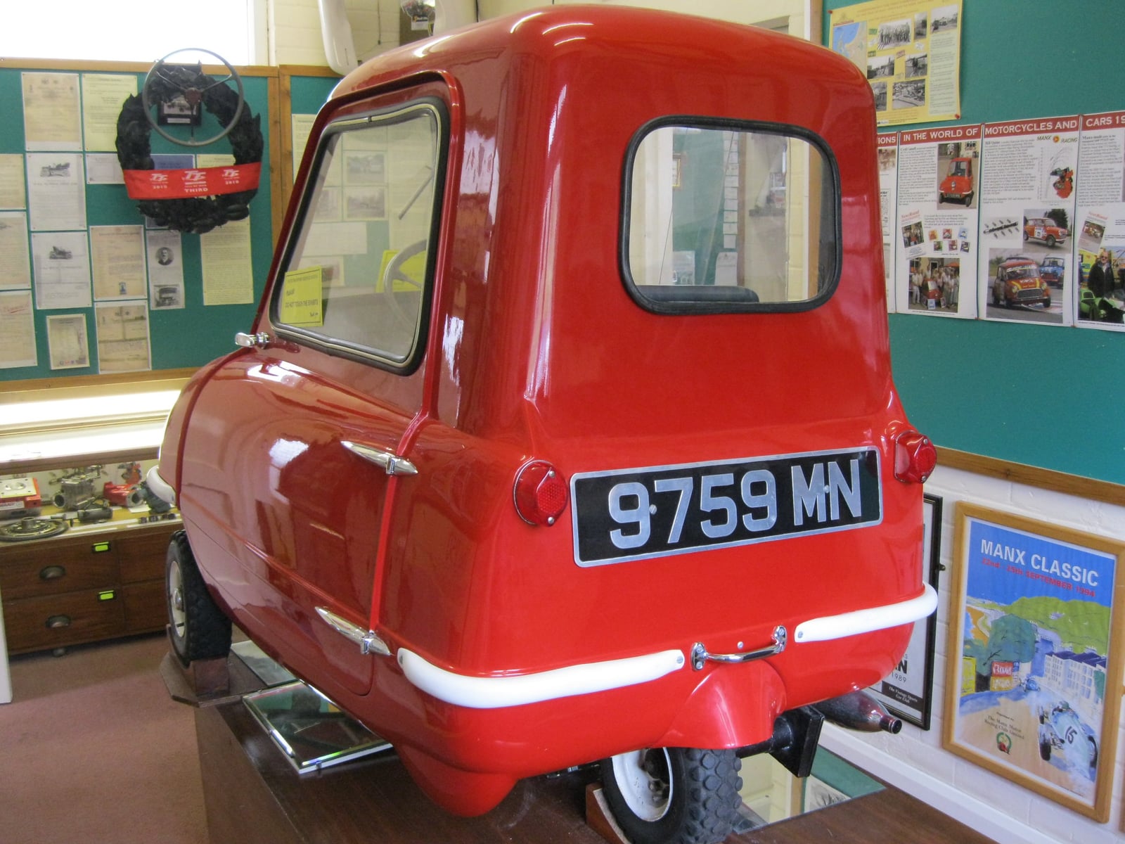 A red Peel P50 three-wheeler seen from the rear in a transport museum, its single rear wheel visible, UK registration 9759 MN