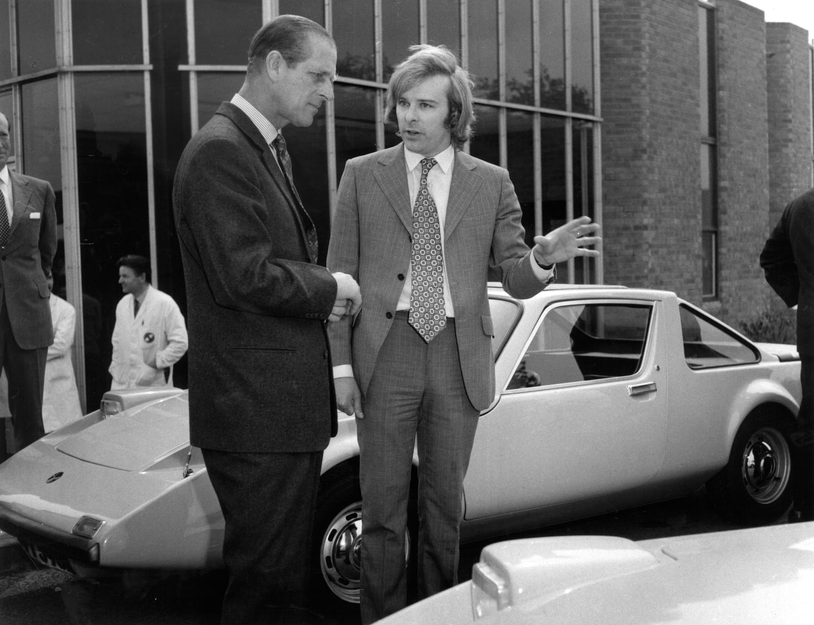 A black and white photograph of Prince Philip talking to a man beside a Clan Crusader at the Clan Motor Company factory