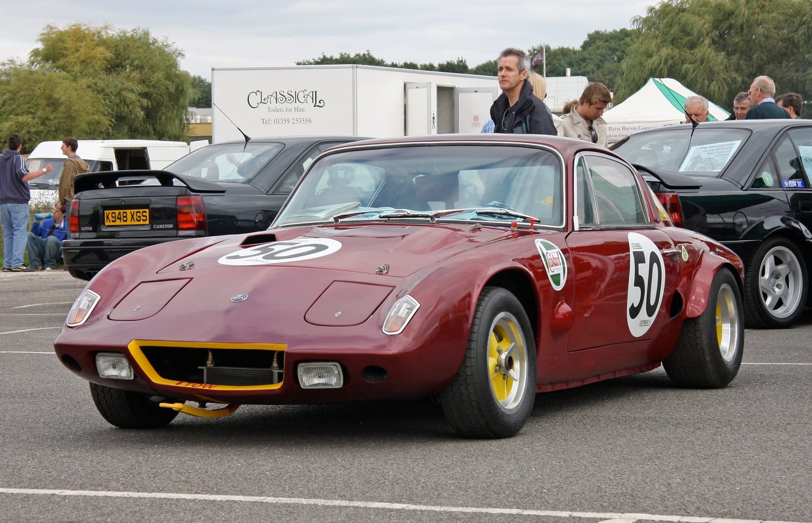 A dark red Lotus Elan competition car carrying race number 50 in a circuit paddock