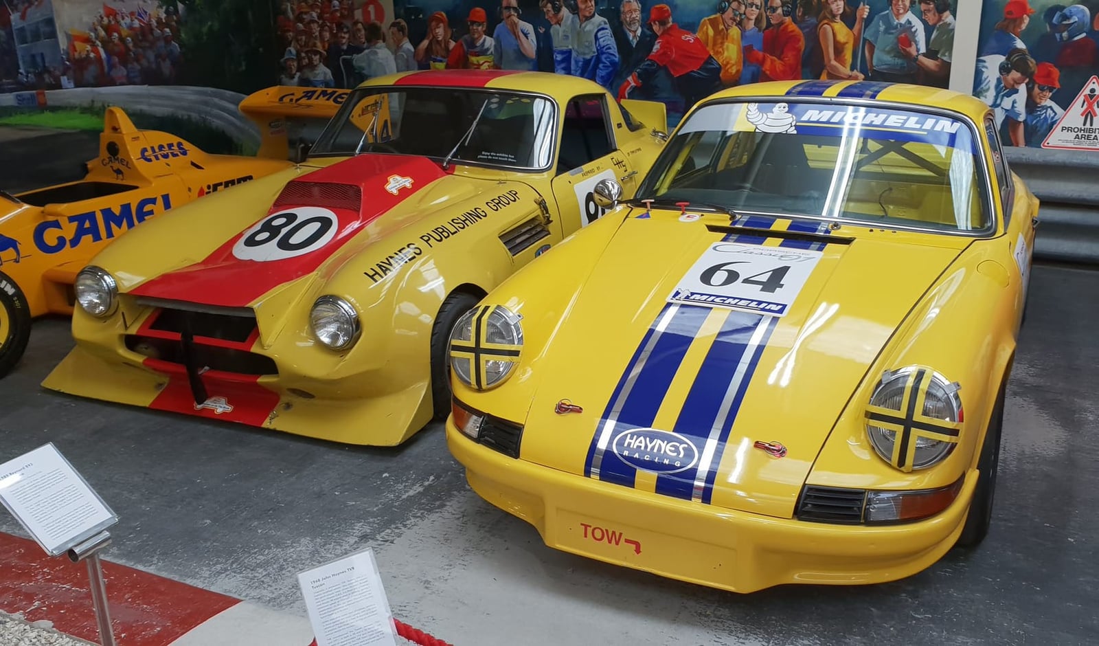 A yellow racing TVR beside a Porsche 911 in a museum display