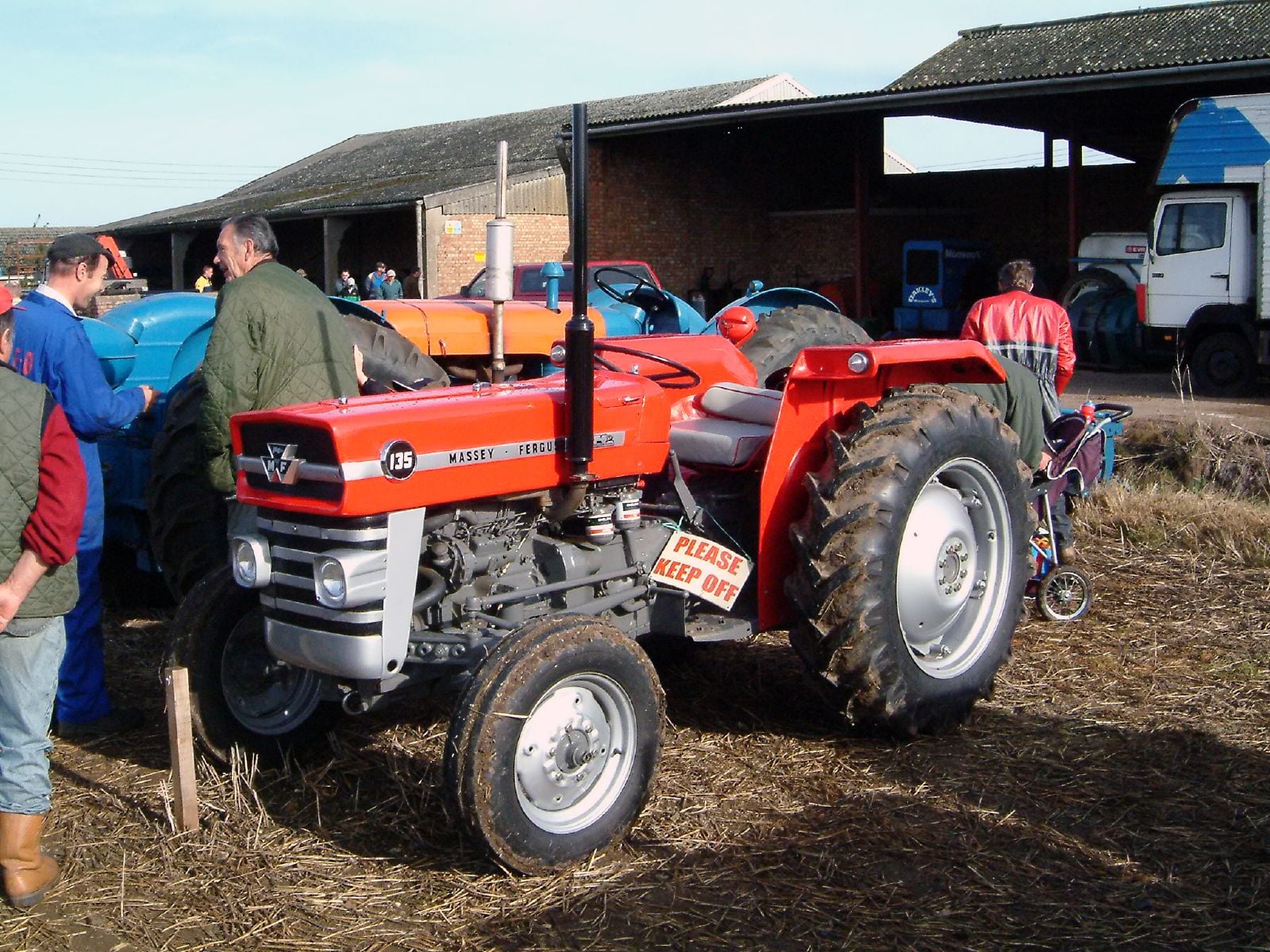 A red Massey Ferguson 135 at a national ploughing championship, people and tractors in a farmyard behind