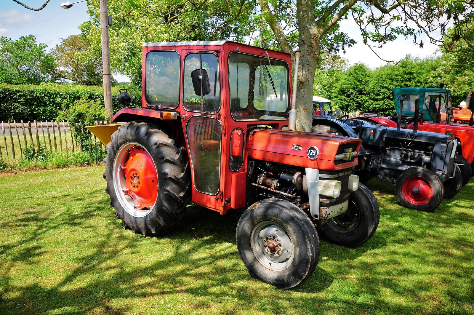 A red Massey Ferguson 135 with a cab parked on grass at a classic tractor and car show