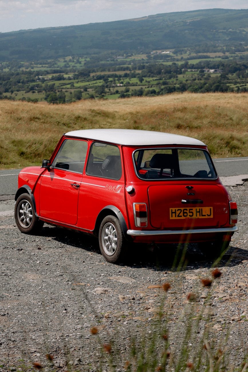 A red Mini Cooper with a white roof on a country road, rear three-quarter view
