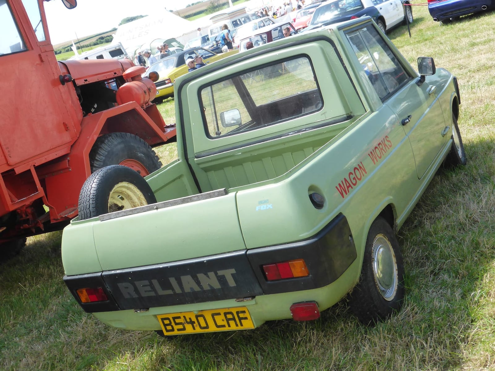 A pale green 1985 Reliant Fox pickup on grass at a vehicle rally, side view showing the open load bed