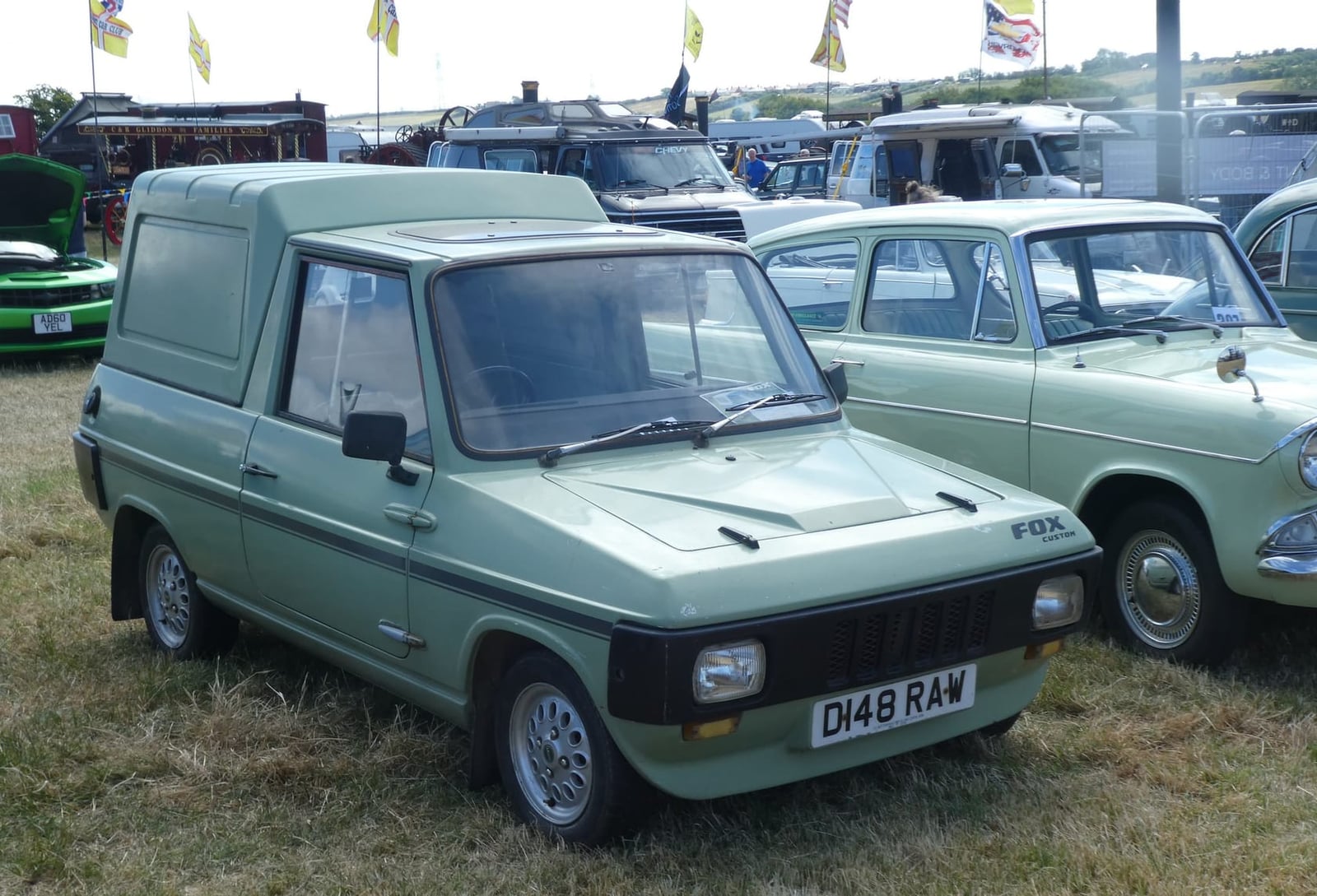 A green Reliant Fox van with a hard top parked at a vehicle show, front three-quarter view, UK registration D148 RAW