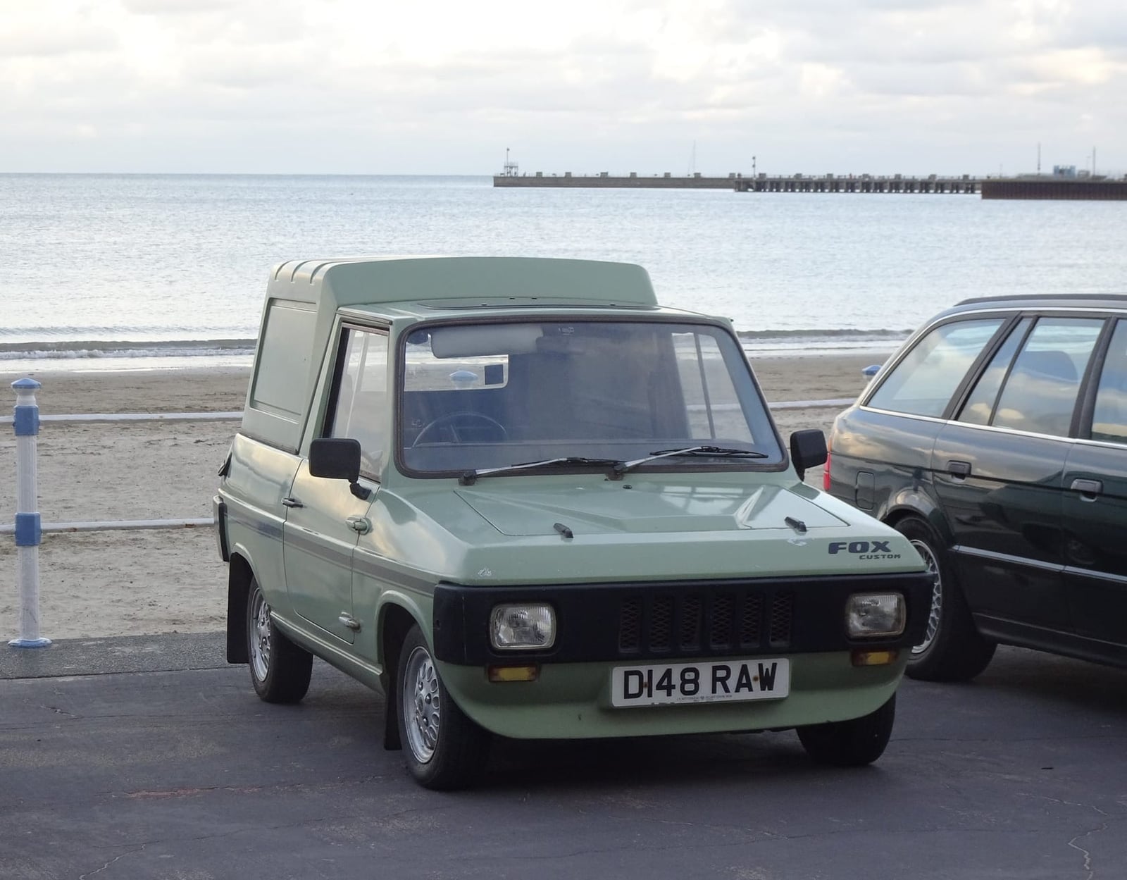 A green Reliant Fox parked on a seafront promenade, front three-quarter view, UK registration D148 RAW