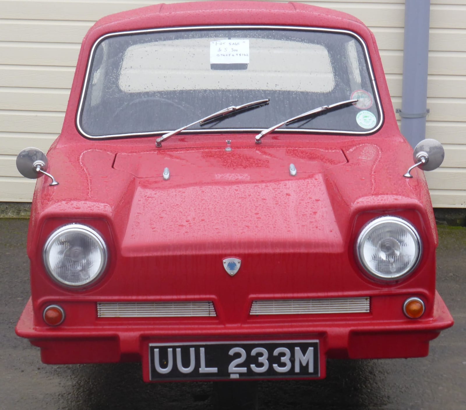 A red Reliant Regal 21E 700 photographed head-on at a classic car show, UK registration UUL 233M
