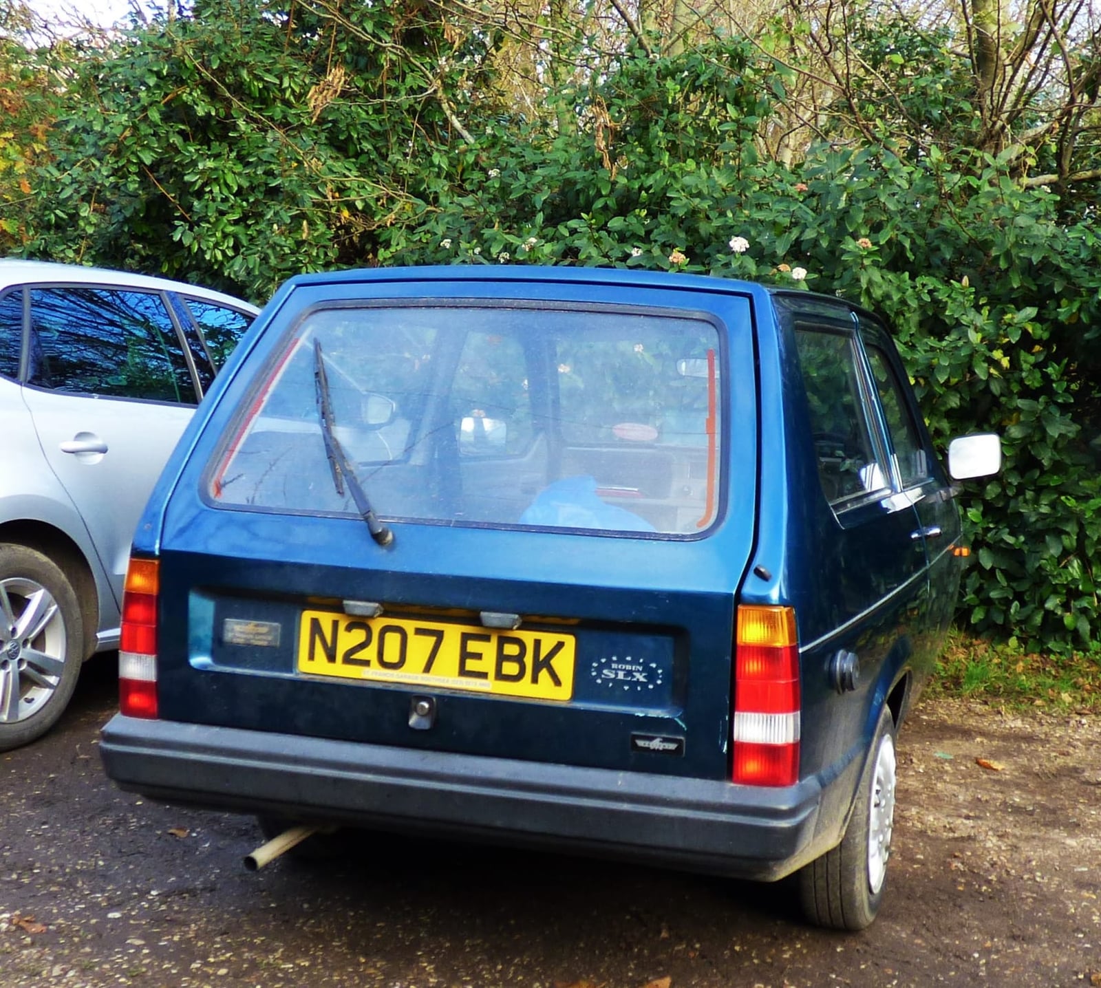 The rear of a dark blue 1995 Reliant Robin SLX parked by a hedge, UK registration N207 EBK