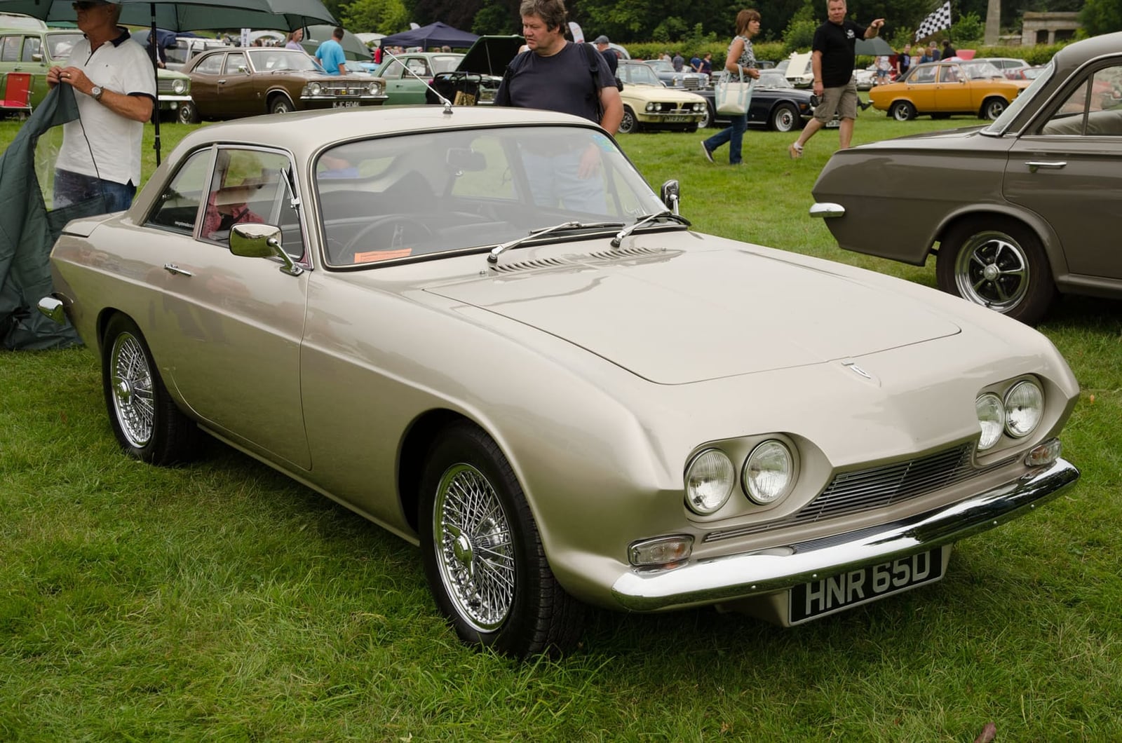 A champagne-coloured 1966 Reliant Scimitar GT SE4 on grass, front three-quarter view, UK registration HNR 66D