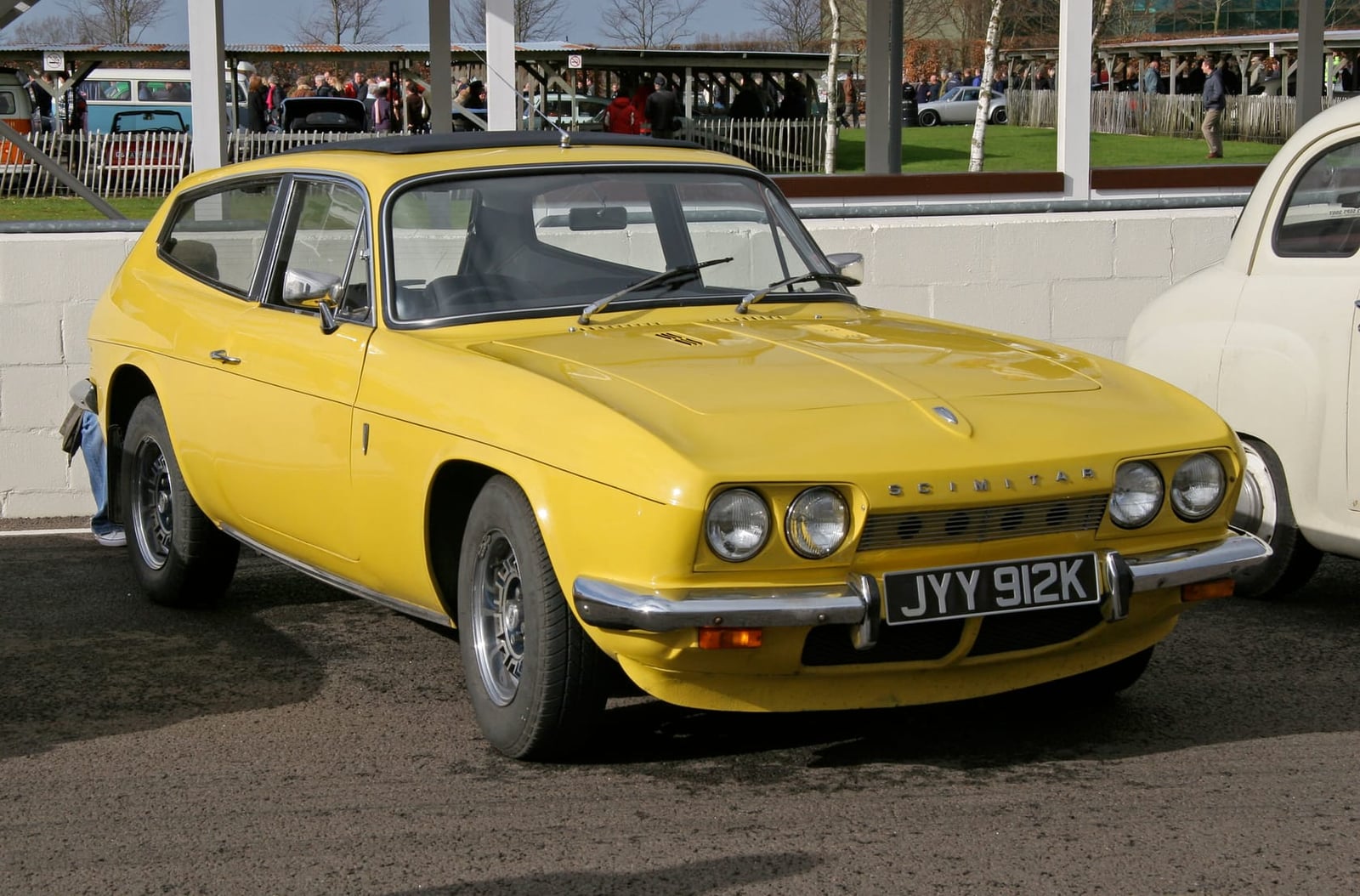 A yellow Reliant Scimitar GTE in a circuit paddock, front three-quarter view, UK registration JYY 912K