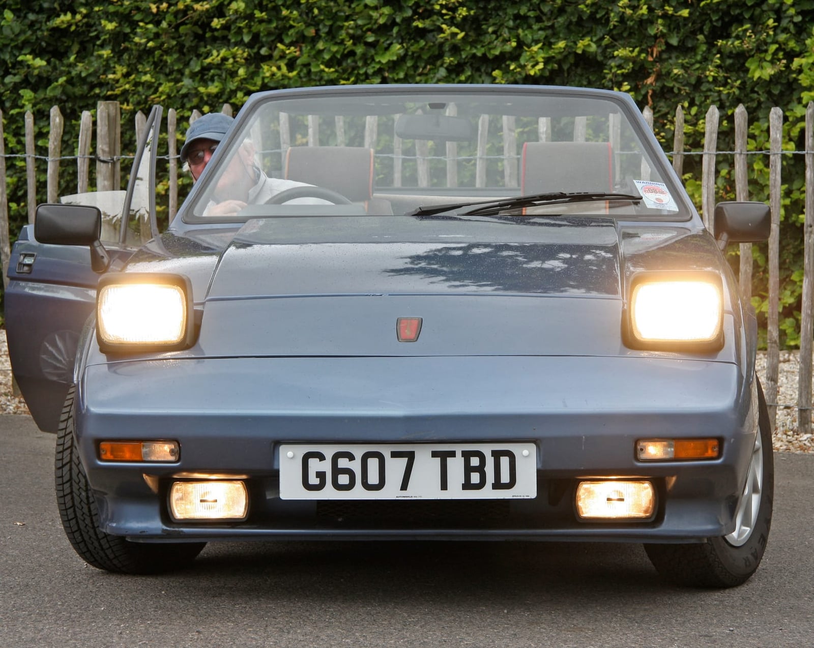 A grey Reliant Scimitar SS1 with its pop-up headlamps raised, photographed head-on