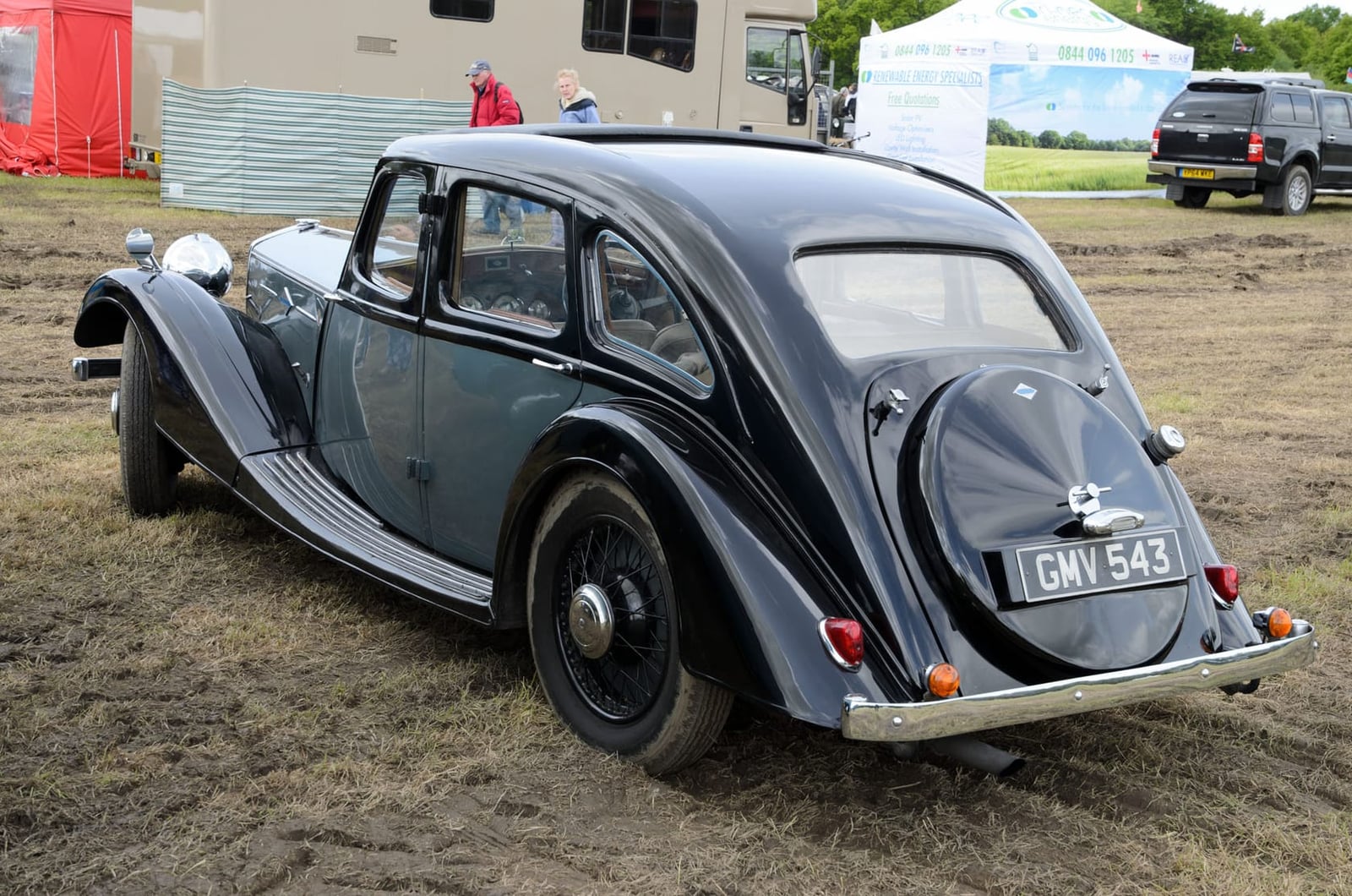 A grey 1938 Riley 16hp Kestrel with a rear-mounted spare wheel on grass at a classic vehicle show, side view, UK registration GMV 543