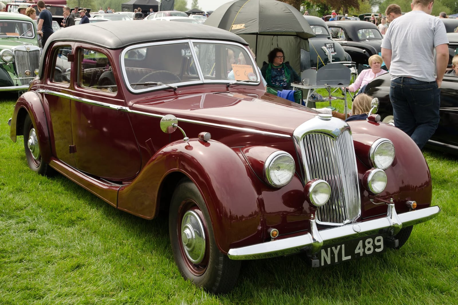 A maroon 1953 Riley RMF 2.5-litre saloon on grass at a show, front three-quarter view, UK registration NYL 489