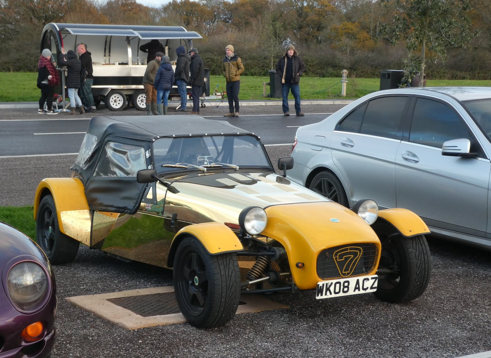 A yellow Robin Hood Seven-style roadster, registration WK08 AC2, on tarmac at an event